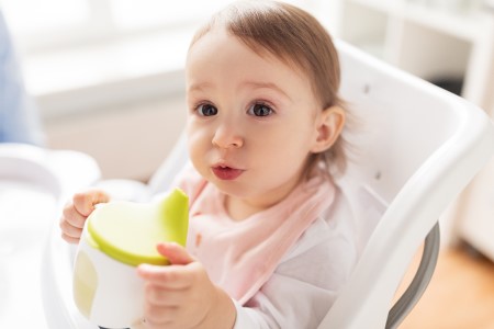 Baby sitting in a high chair holding a sippy cup